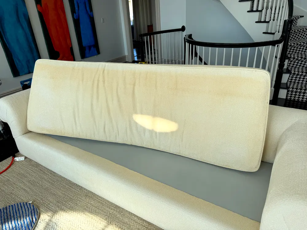 Vertical browning streaks on a cotton and linen sofa cushion after improper cleaning.