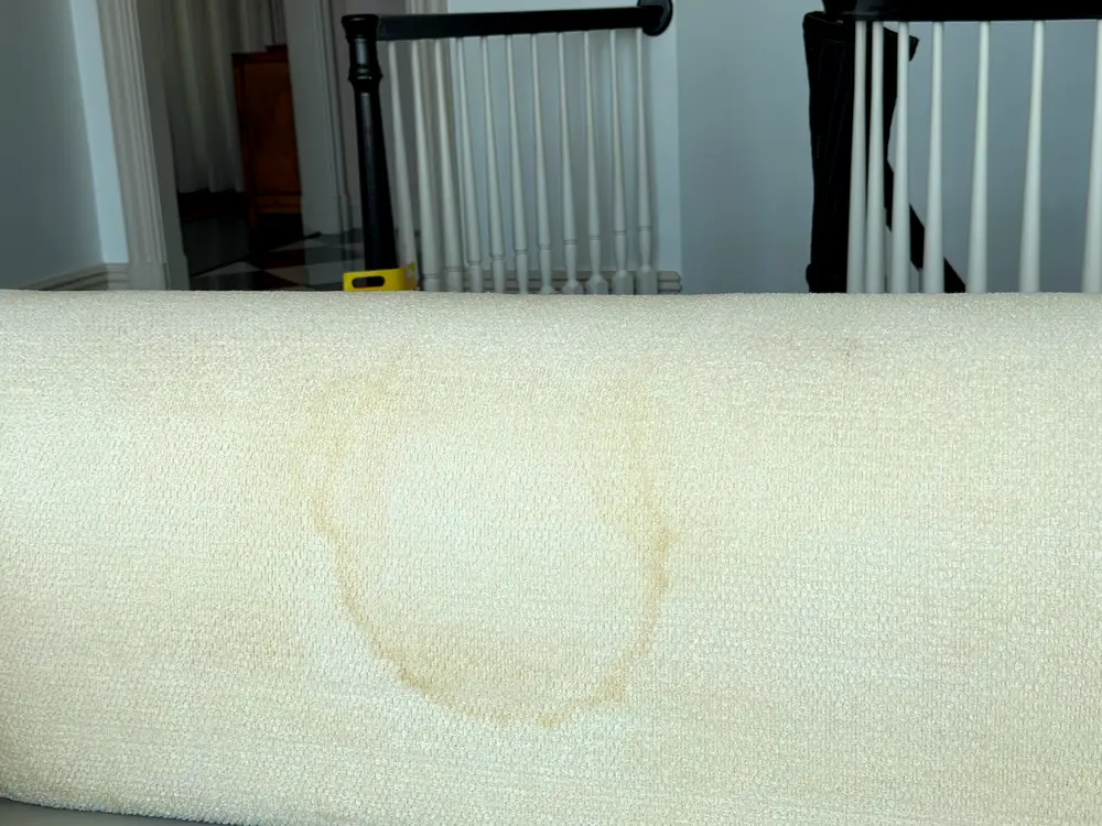 Brown ring on the roll arm of a cotton and linen sofa caused by overwetting.
